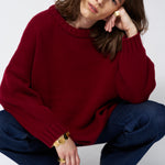 a woman in a red sweater and jeans in front of white wall
