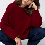 a woman in a red sweater and jeans in front of white wall
