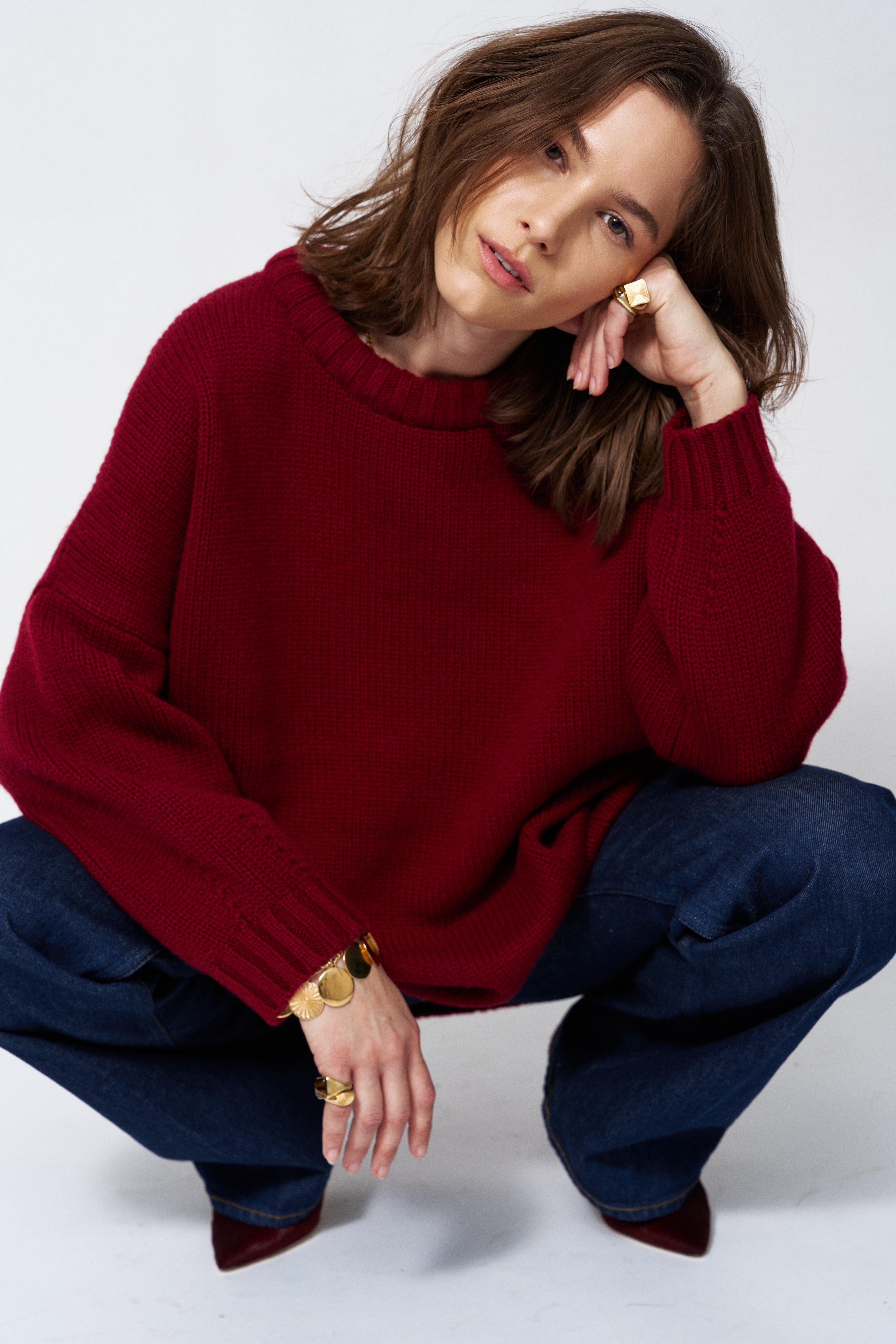 a woman in a red sweater and jeans in front of white wall
