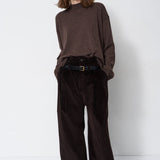 A model stands against a plain white studio background wearing a dark brown mock-neck knit sweater, dark brown wide-leg corduroy trousers, and a black belt.