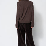 A model shown from the back wearing a dark brown knit long-sleeve top and dark brown wide-leg corduroy trousers against a plain white studio background.