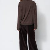 A model shown from the back wearing a dark brown knit long-sleeve top and dark brown wide-leg corduroy trousers against a plain white studio background.