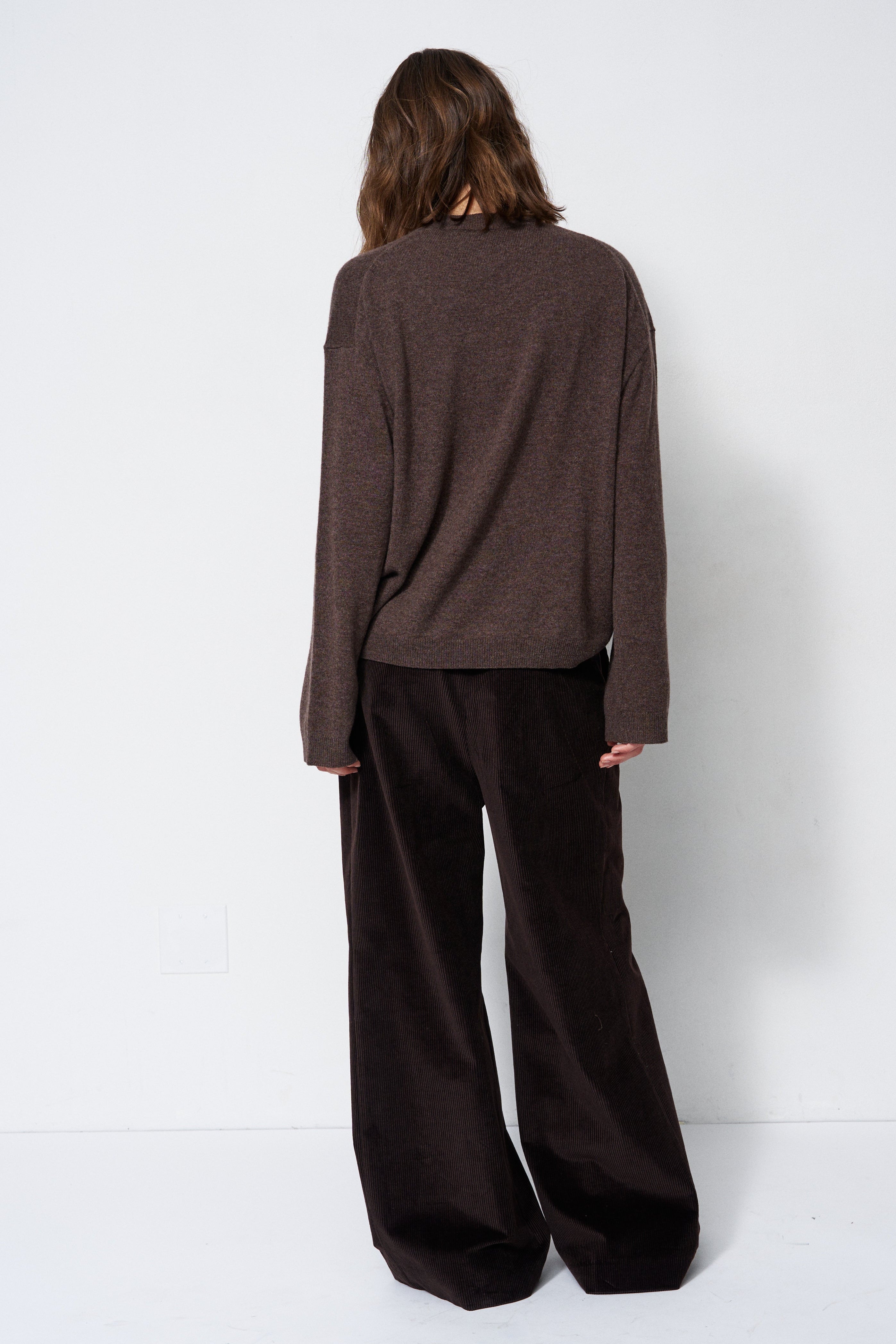A model shown from the back wearing a dark brown knit long-sleeve top and dark brown wide-leg corduroy trousers against a plain white studio background.