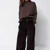 A woman modeling a dark brown knit mock-neck sweater and matching dark brown wide-leg corduroy trousers, styled with a black belt and black shoes, against a plain white studio background.