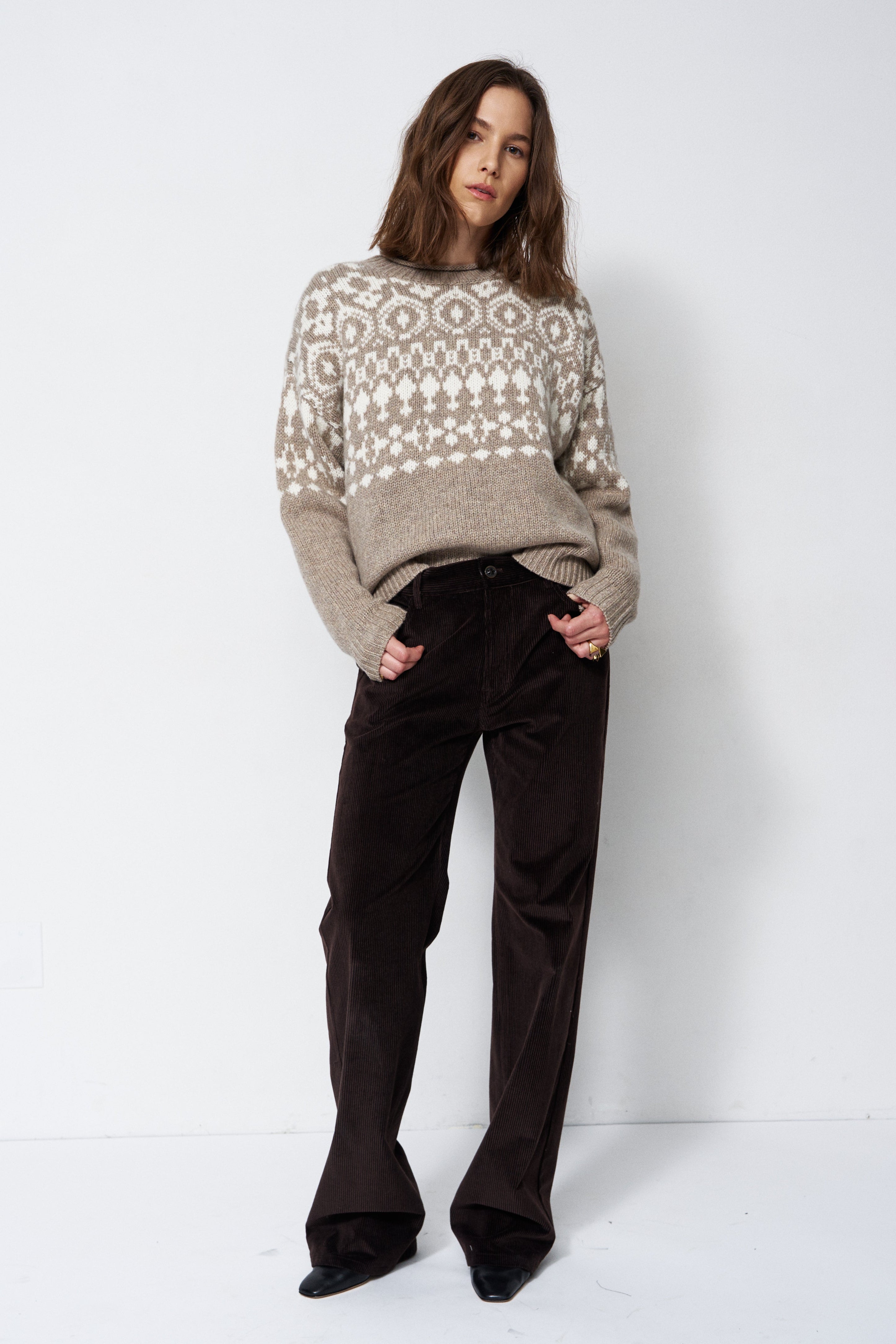model standing with white background in grey and white sweater
