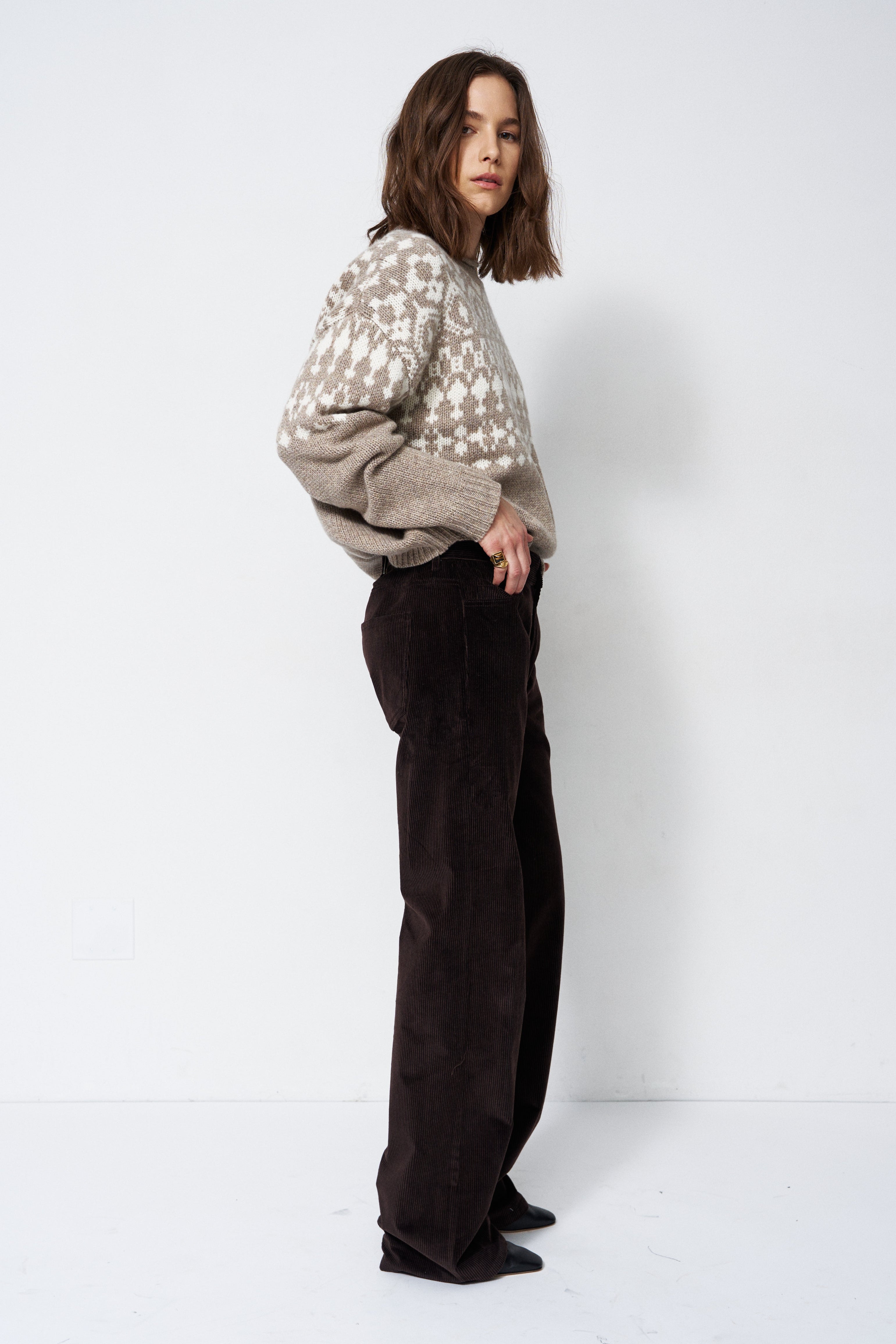 model standing in grey and white sweater with white background
