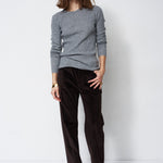 A woman modeling a light gray knit crewneck sweater and dark brown wide-leg corduroy trousers against a plain white studio background.