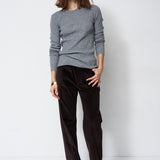 A woman modeling a light gray knit crewneck sweater and dark brown wide-leg corduroy trousers against a plain white studio background.