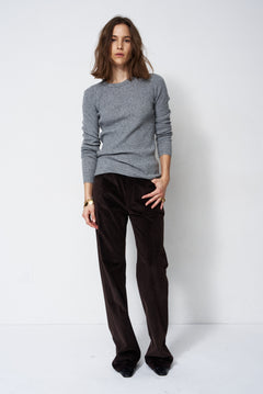 A woman modeling a light gray knit crewneck sweater and dark brown wide-leg corduroy trousers against a plain white studio background.