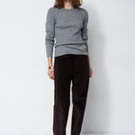 A woman modeling a gray knit crewneck sweater and dark brown corduroy trousers against a plain white studio background.
