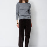 A woman modeling a gray knit crewneck sweater and dark brown corduroy trousers against a plain white studio background.