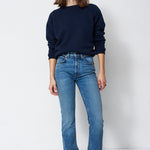 woman in navy sweatshirt and jeans in front of a white wall