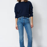 woman in navy sweatshirt and jeans in front of a white wall