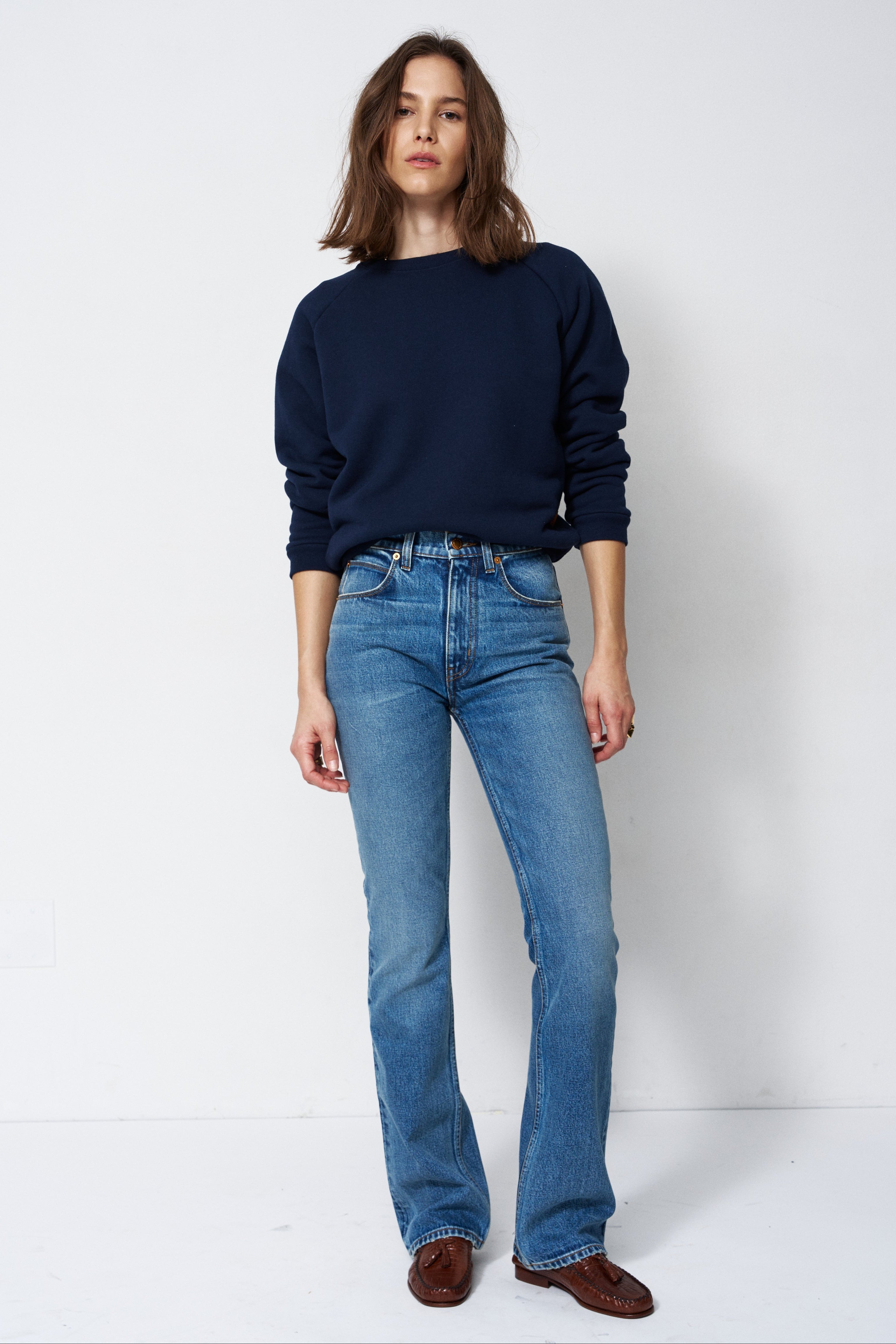 woman in navy sweatshirt and jeans in front of a white wall
