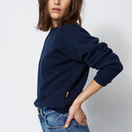 woman in navy sweatshirt and jeans in front of a white wall
