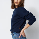 woman in navy sweatshirt and jeans in front of a white wall
