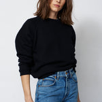 woman in a black sweatshirt and jeans in front of a white wall