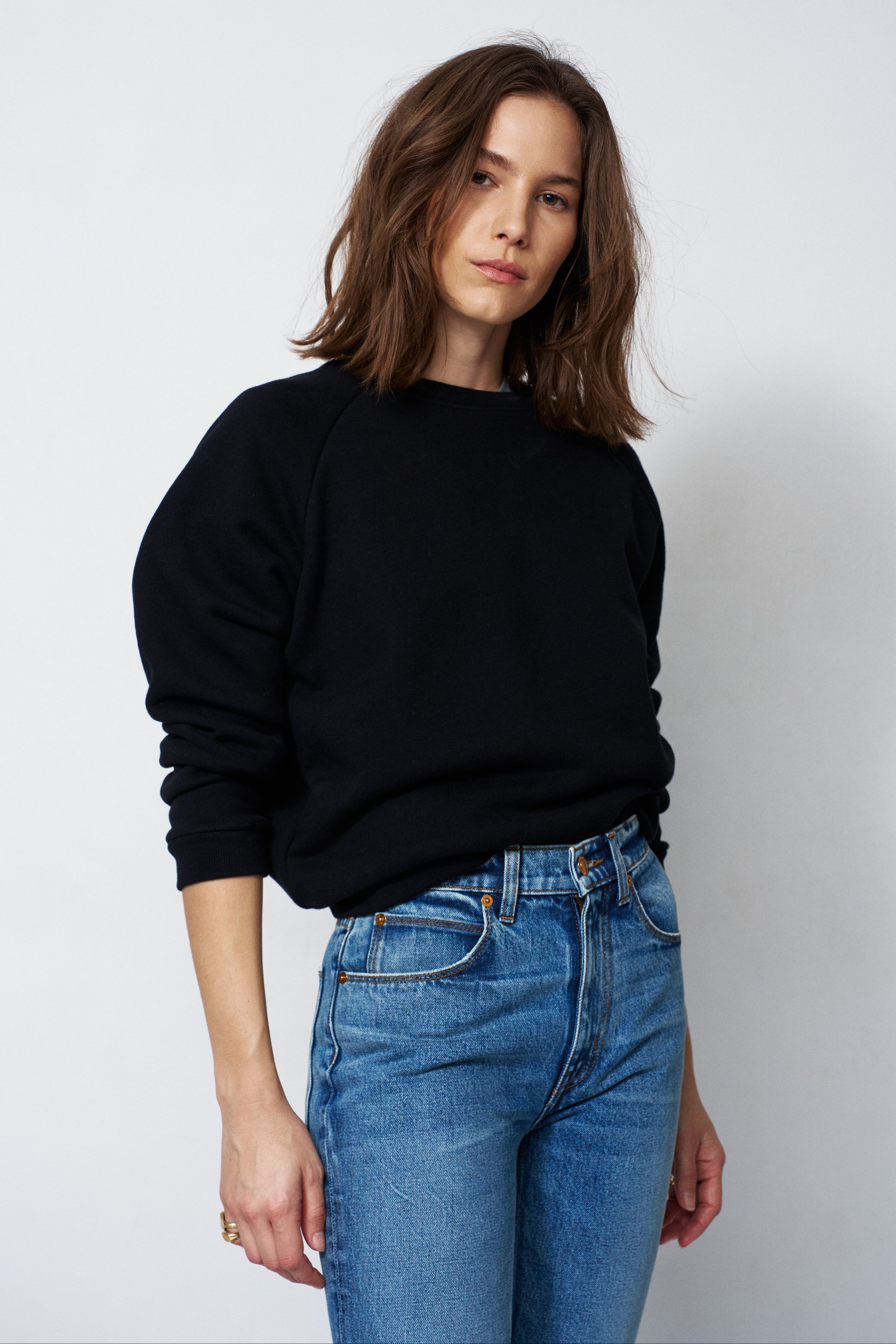 woman in a black sweatshirt and jeans in front of a white wall