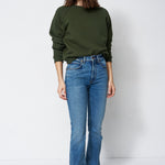 woman in green sweatshirt and jeans in front of a white wall