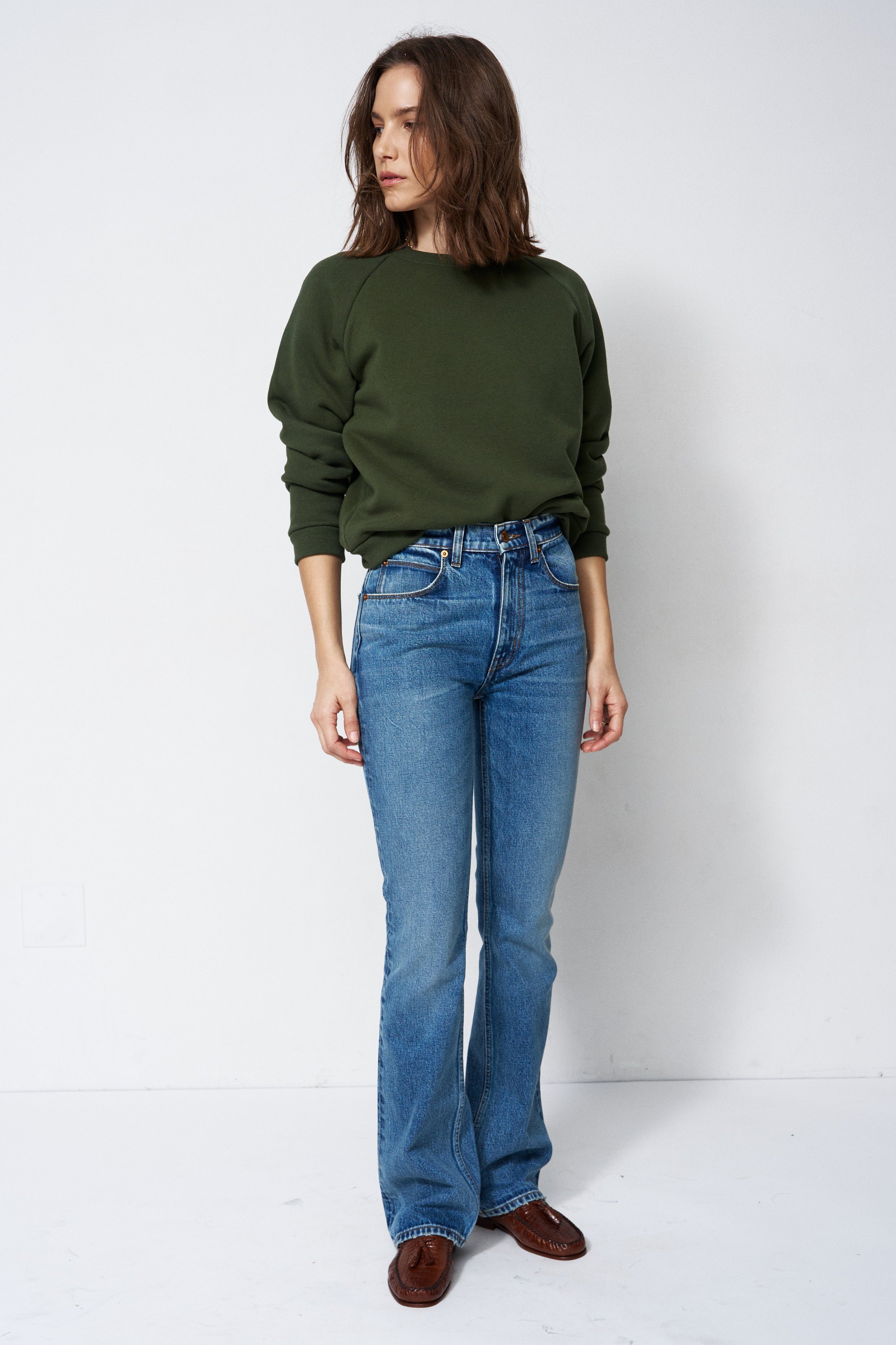 woman in green sweatshirt and jeans in front of a white wall