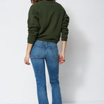 woman in green sweatshirt and jeans in front of a white wall