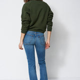 woman in green sweatshirt and jeans in front of a white wall