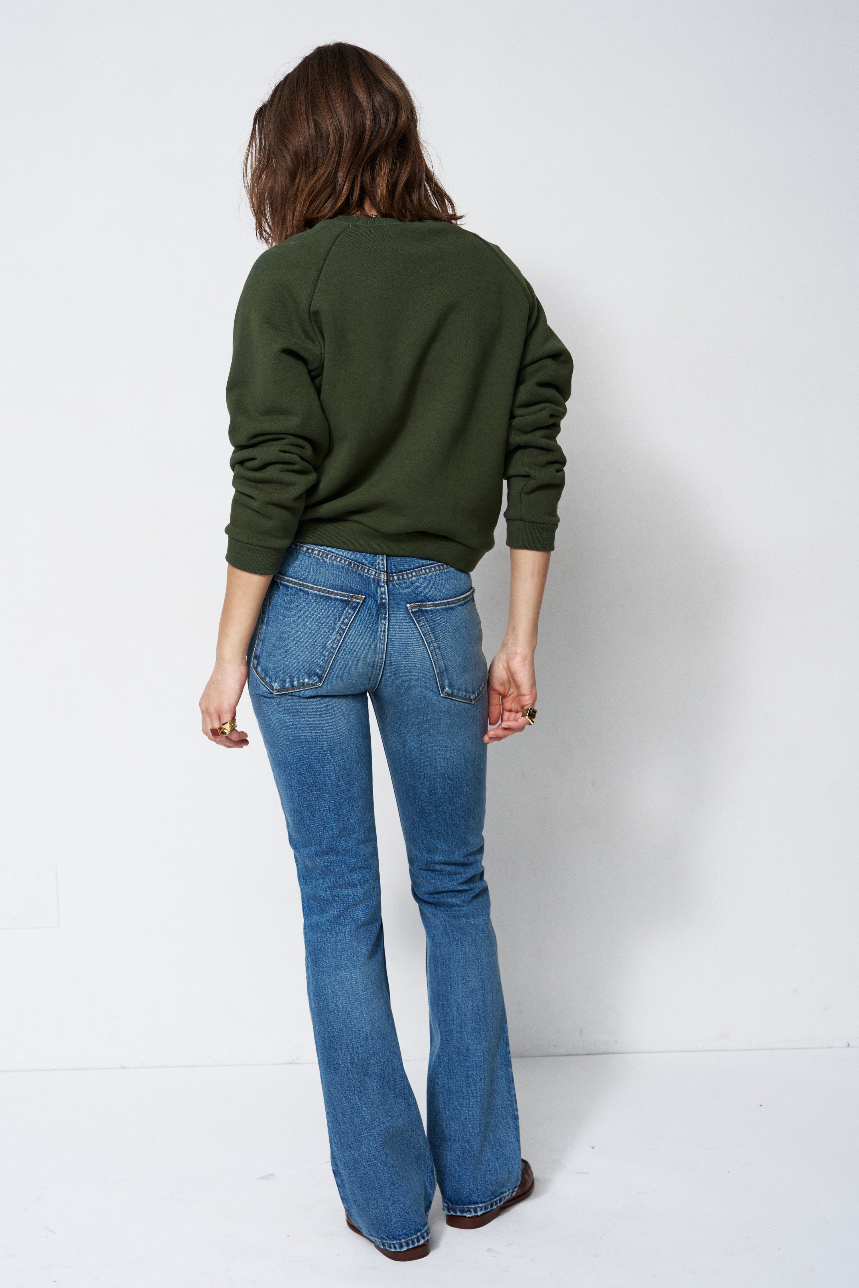 woman in green sweatshirt and jeans in front of a white wall