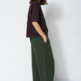 model in green pants and brown shirt standing in front of a white wall