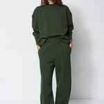woman in green sweatshirt and pants in front of a white wall