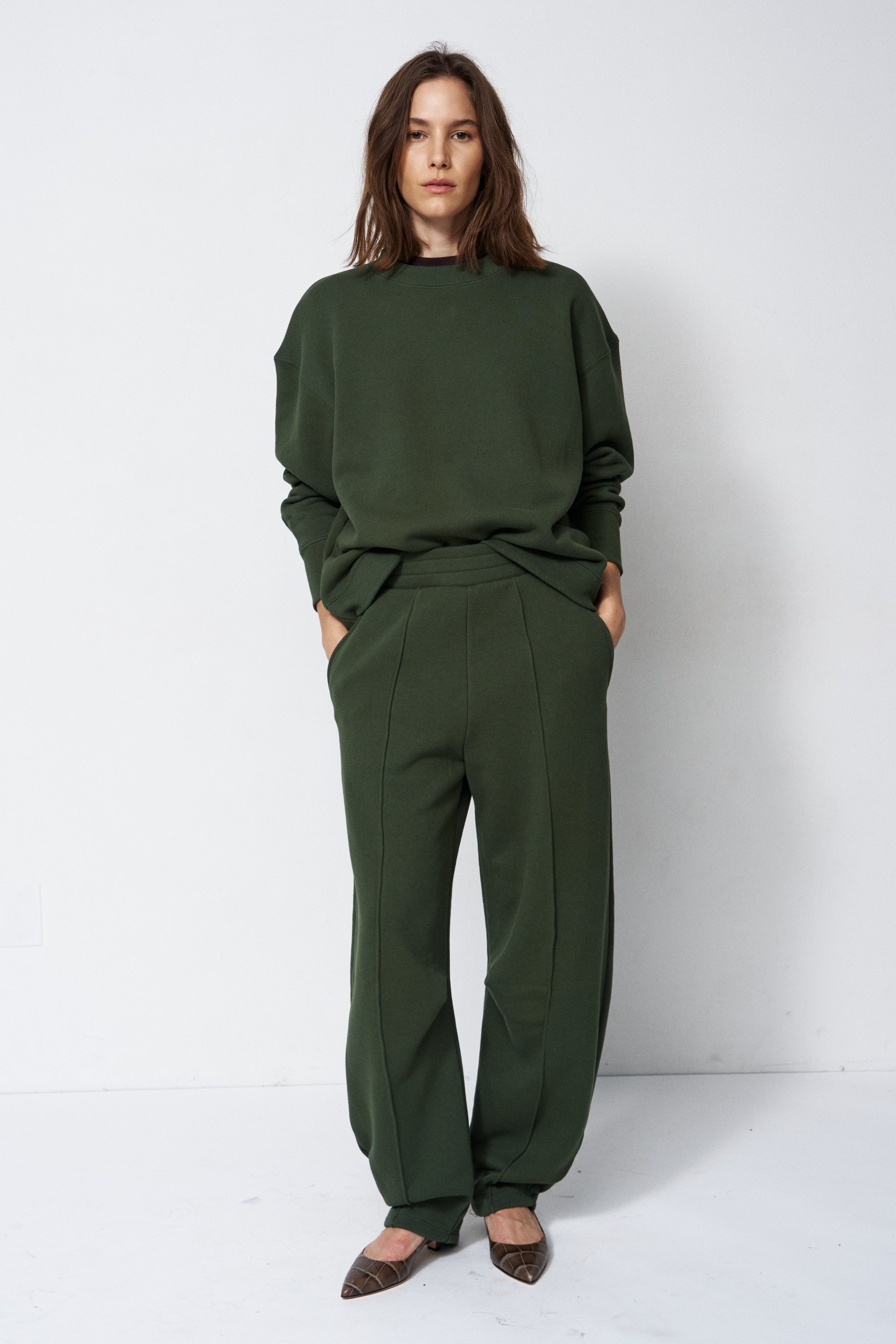 woman in green sweatshirt and pants in front of a white wall