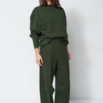 woman in green sweatshirt and pants in front of a white wall