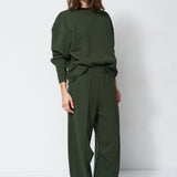woman in green sweatshirt and pants in front of a white wall
