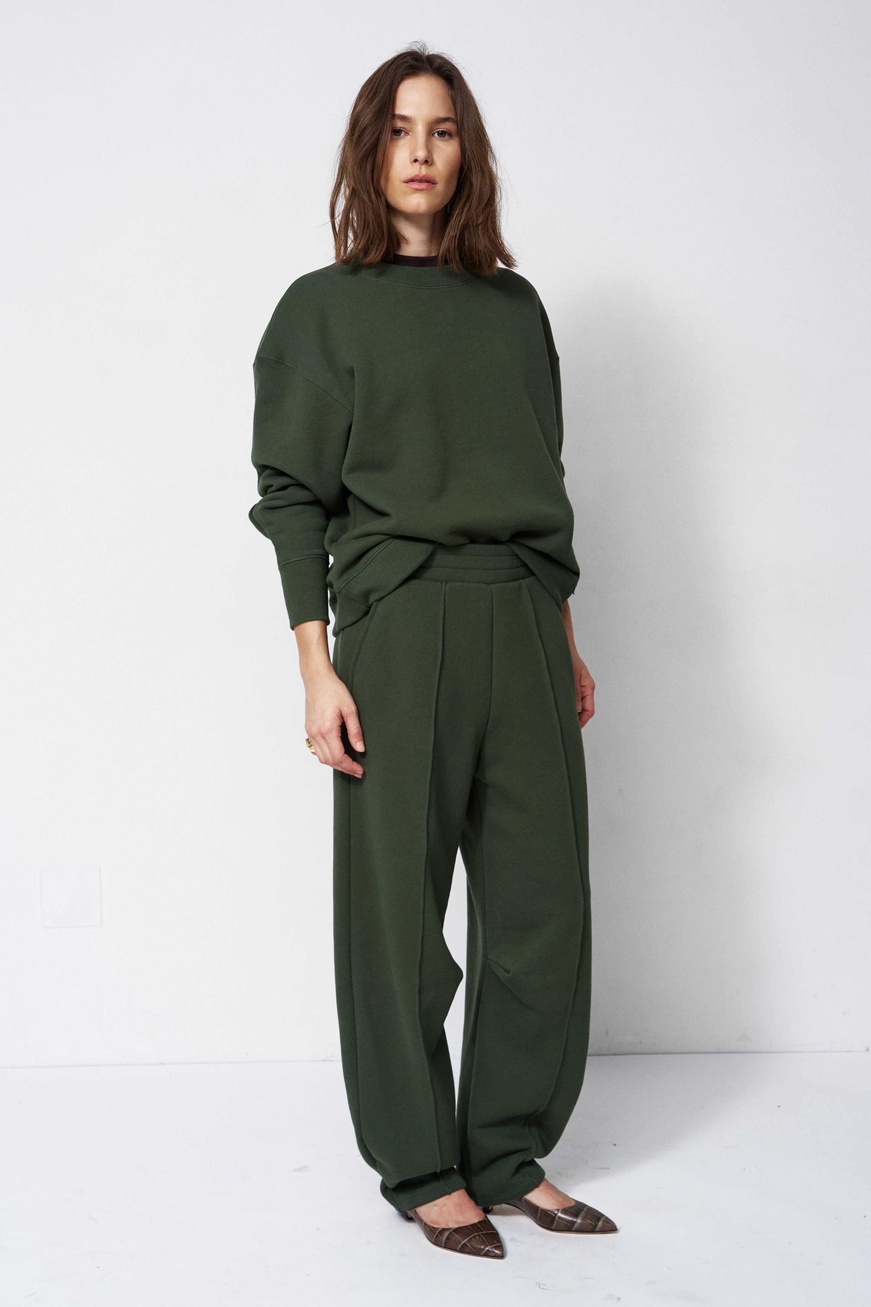 woman in green sweatshirt and pants in front of a white wall