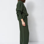 woman in green sweatshirt and pants in front of a white wall