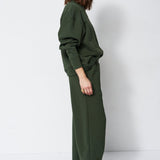 woman in green sweatshirt and pants in front of a white wall