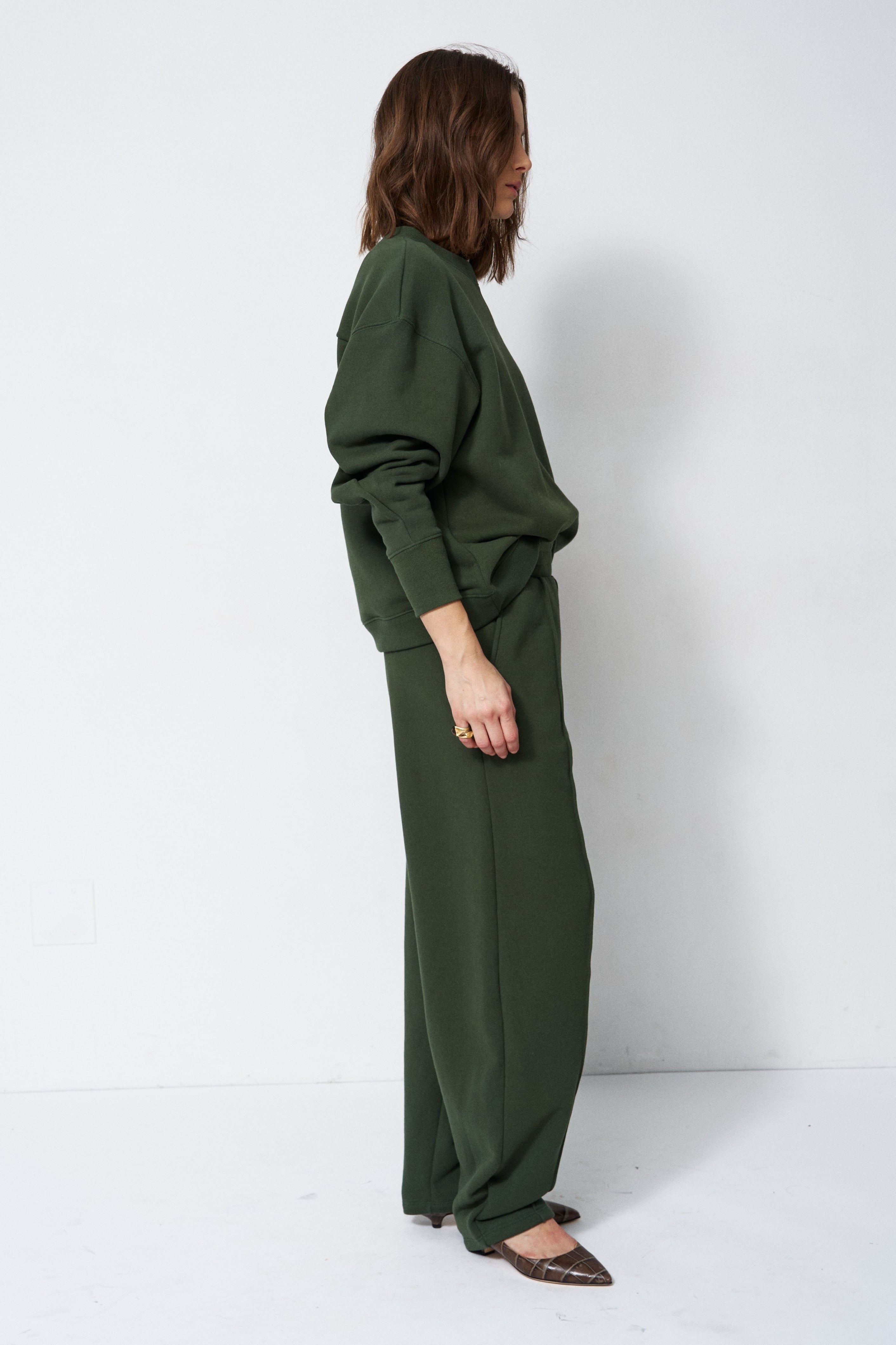 woman in green sweatshirt and pants in front of a white wall