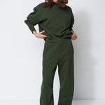 woman in all green sweatsuit standing in front of a white wall