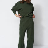 woman in all green sweatsuit standing in front of a white wall