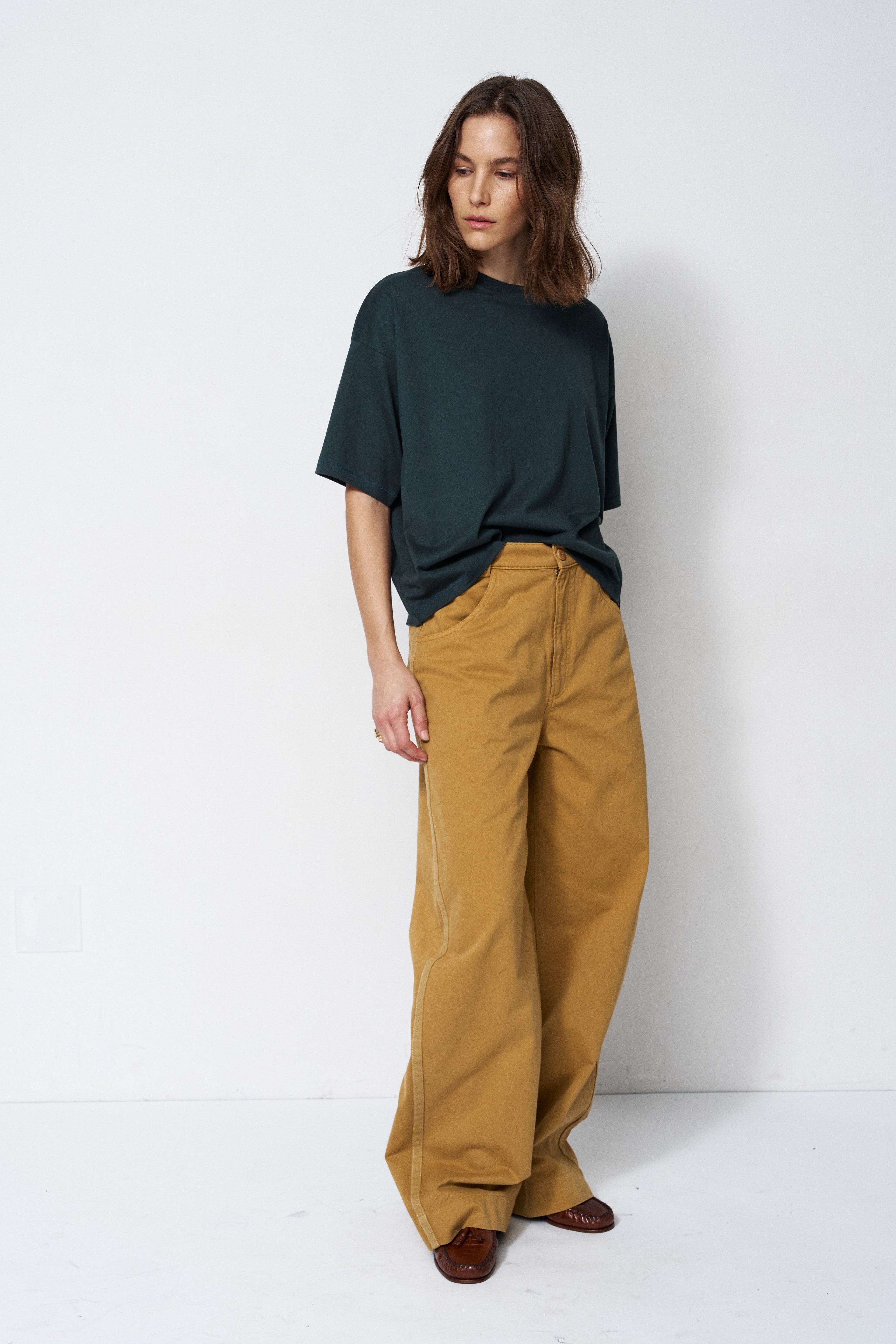 Person wearing a dark green t-shirt and mustard yellow pants against a white background