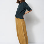 Person wearing a dark green shirt and mustard yellow pants against a white background