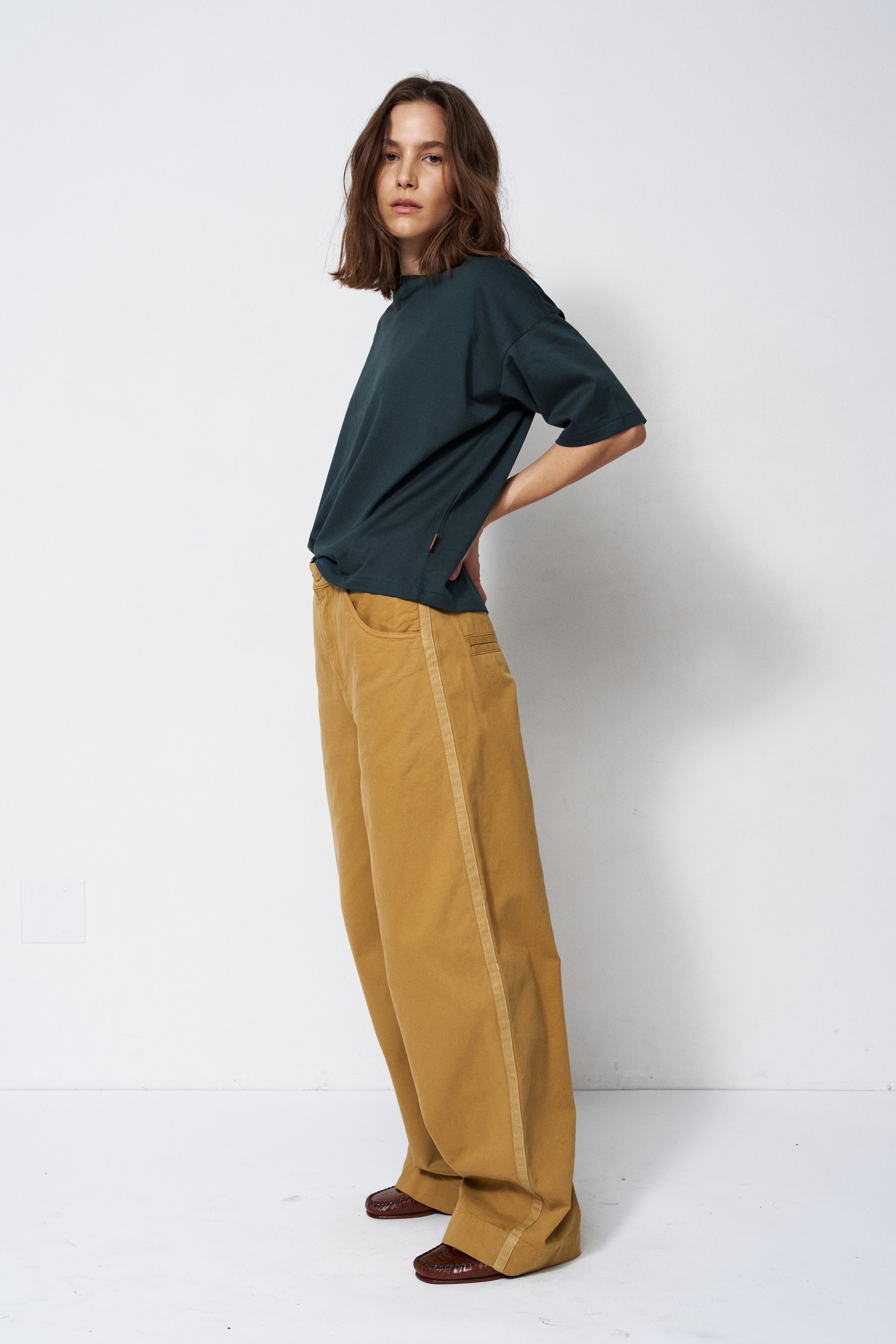 Person wearing a dark green shirt and mustard yellow pants against a white background