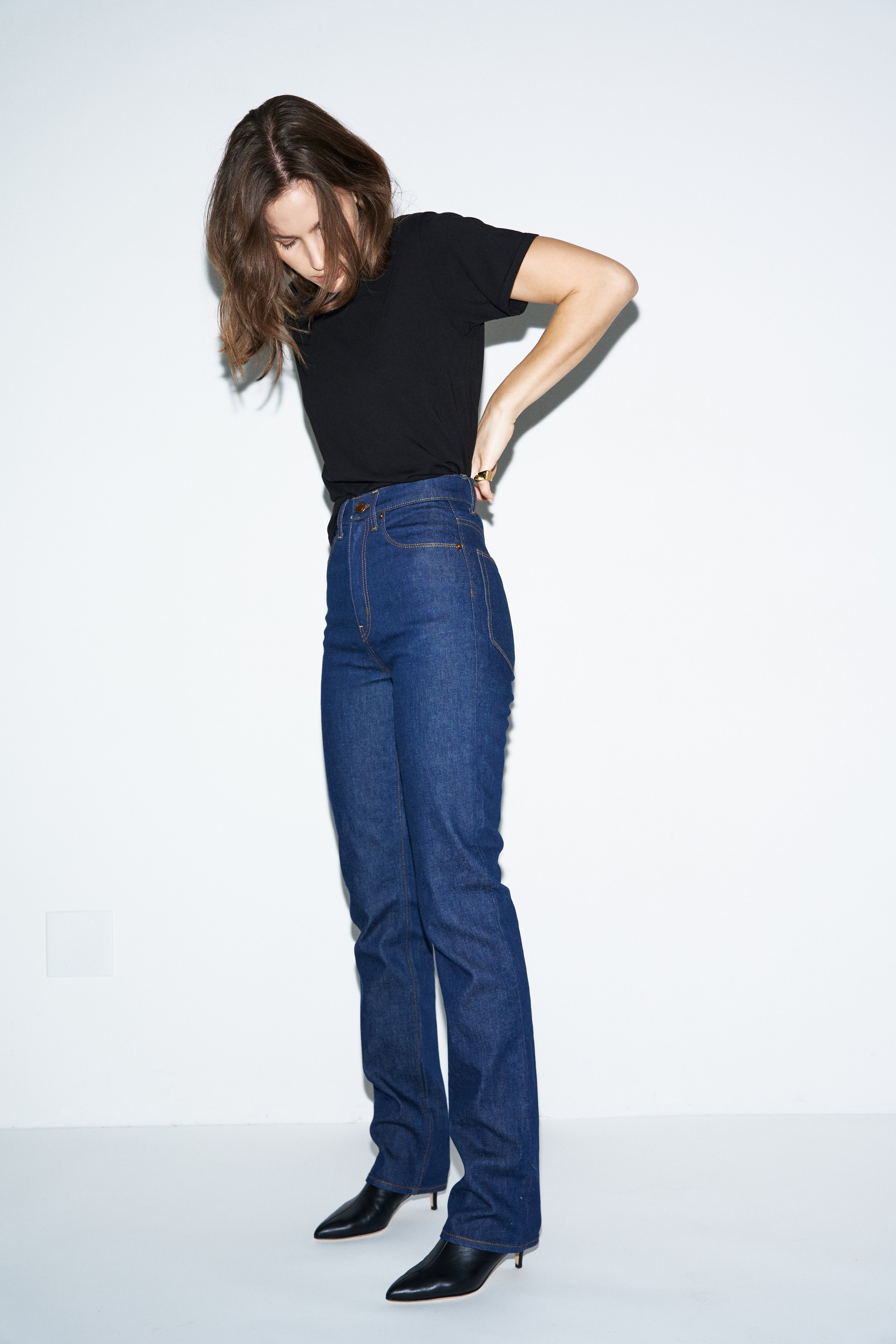 Person wearing blue jeans and a black top on a white background