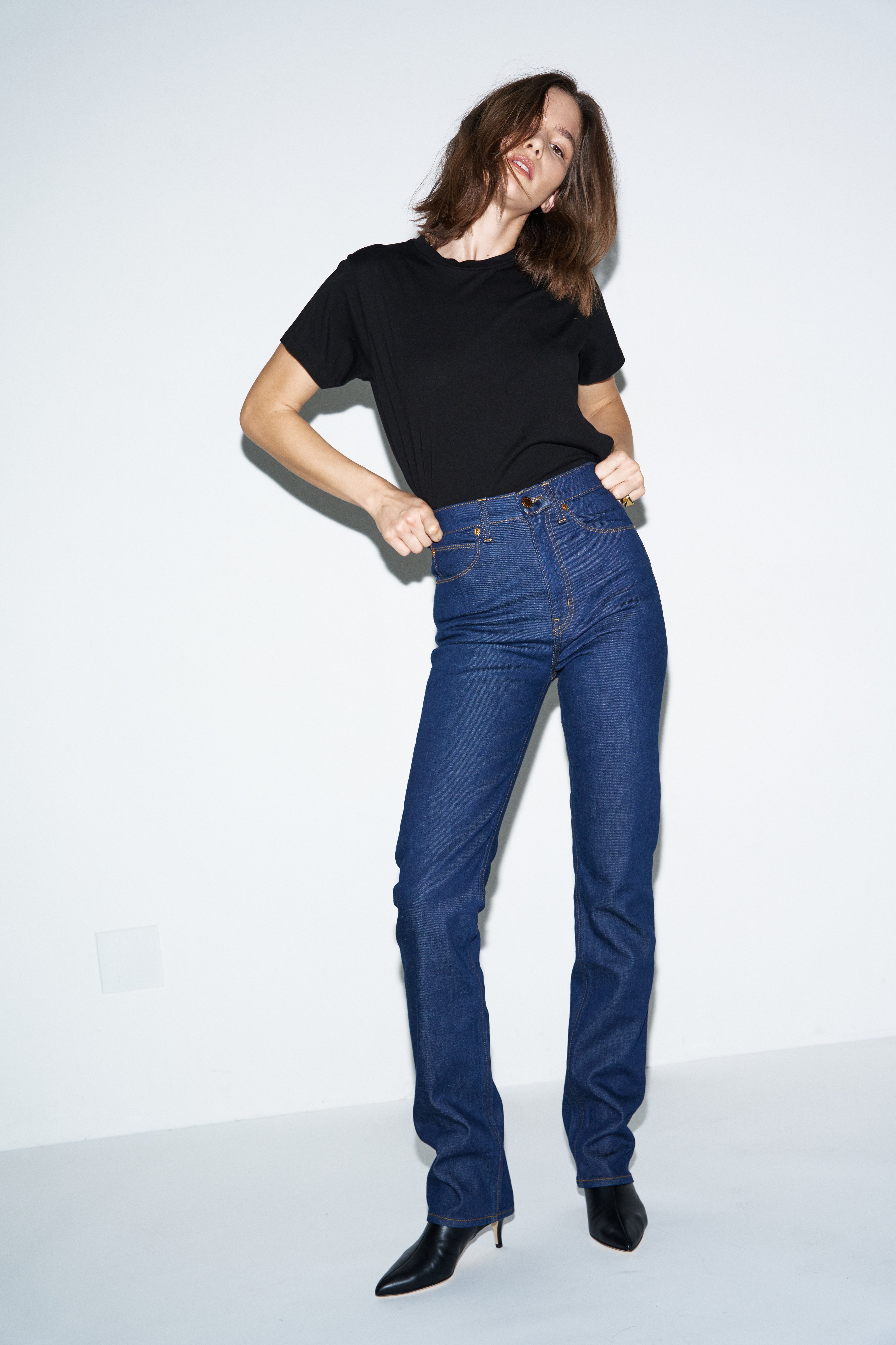 Woman wearing blue jeans and a black top on a white background