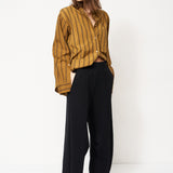 woman in black pants and golden blouse standing in front of a white wall