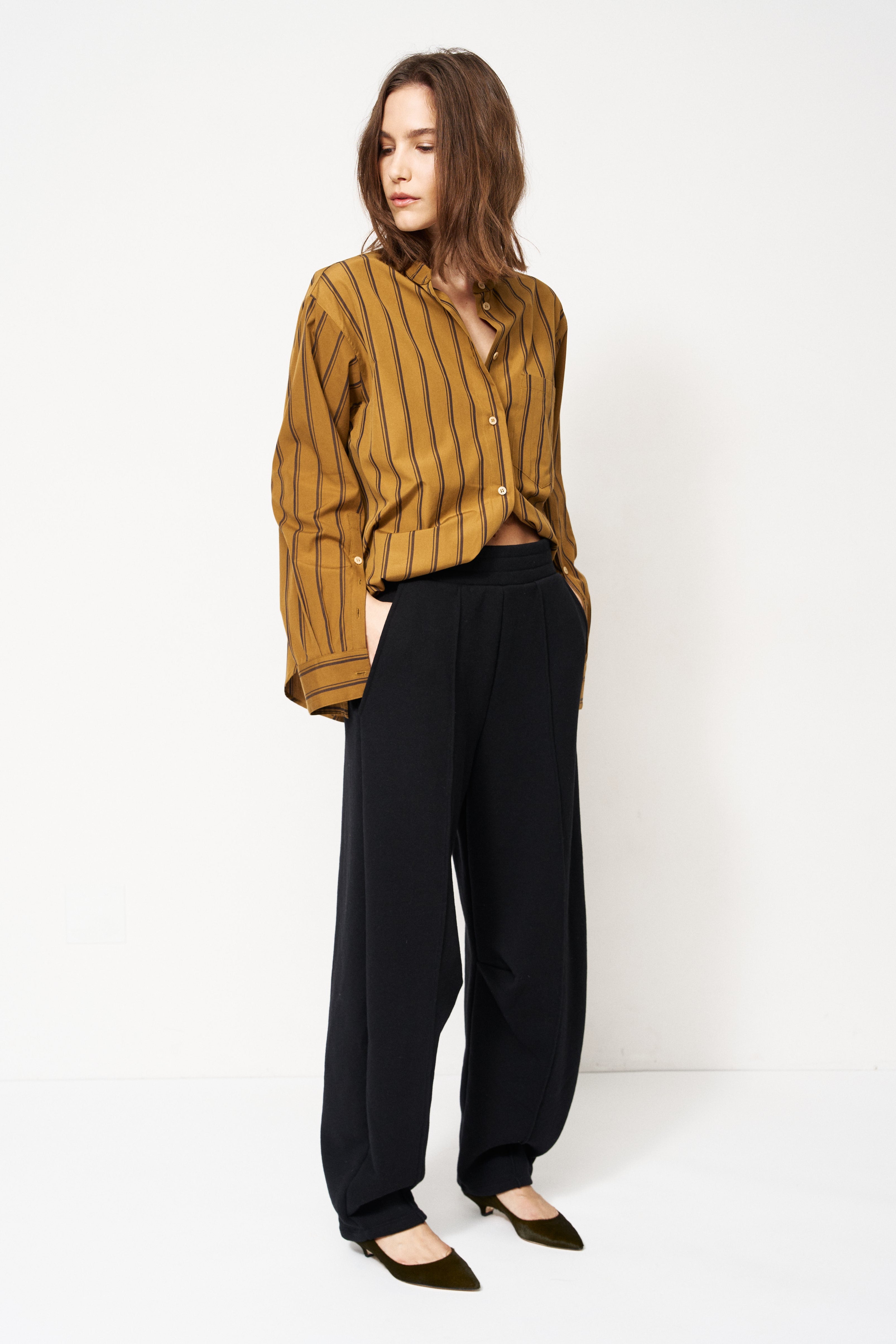 woman in black pants and golden blouse standing in front of a white wall