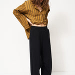woman in black pants and golden blouse standing in front of a white wall