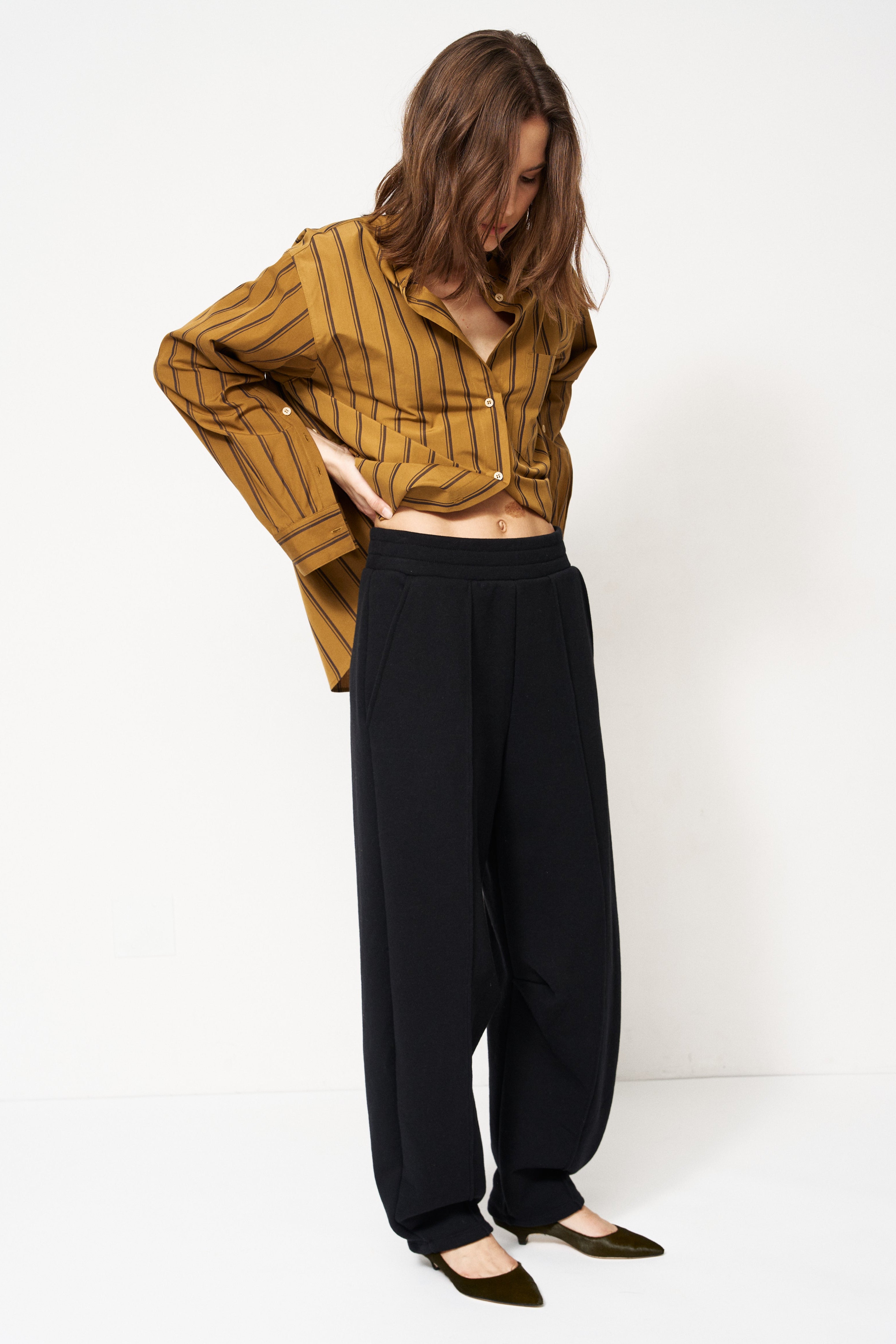 woman in black pants and golden blouse standing in front of a white wall