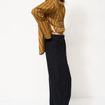 woman in black pants and golden blouse standing in front of a white wall