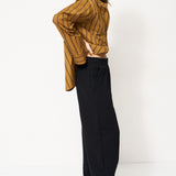 woman in black pants and golden blouse standing in front of a white wall