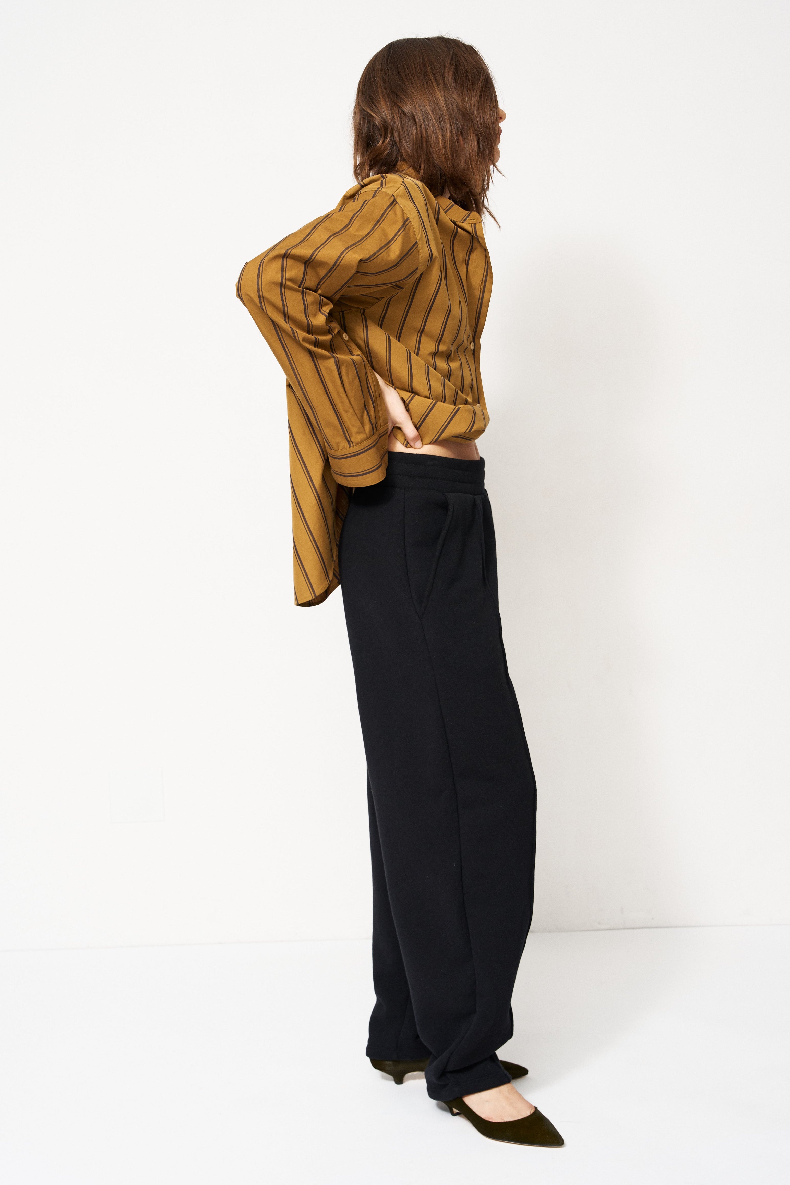 woman in black pants and golden blouse standing in front of a white wall